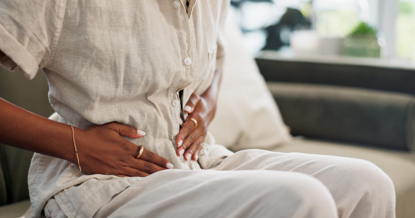 Stomach pain, woman and hands on couch at home with abdomen problem and constipation from virus. Sick person, menstruation and bloated belly ache from colon health issue and cramps in a living room.
